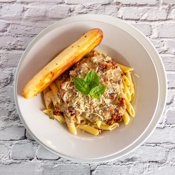 Creamy penne pasta with sun-dried tomatoes, basil, and a breadstick on a white plate.