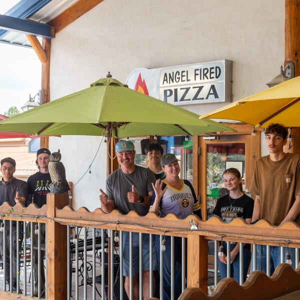 Angel Fired Pizza staff, a group of seven people, smiling on the restaurant's outdoor patio.