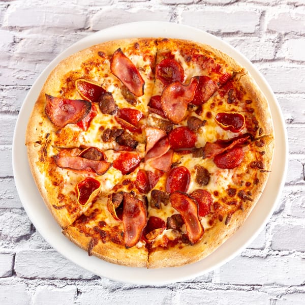 Angel Fired Pizza's meat lover's pizza, topped with pepperoni, bacon, and sausage on a white plate.