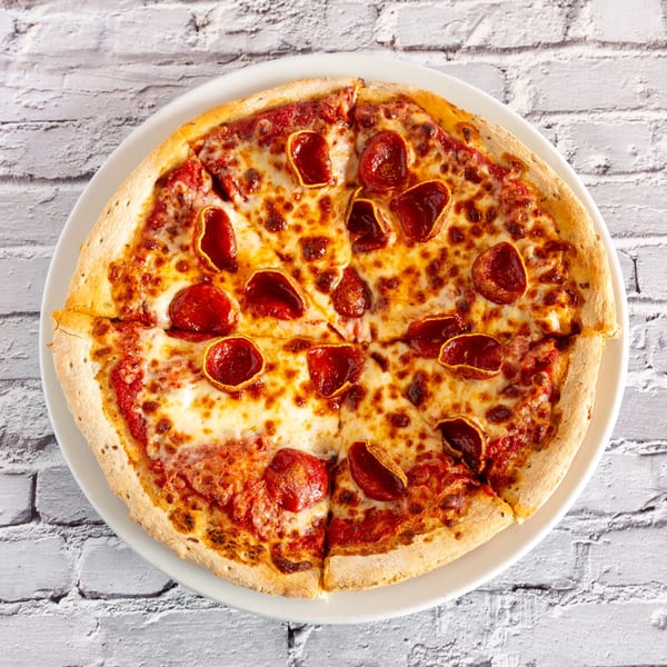 Angel Fired Pizza pepperoni pizza, sliced and served on a white plate against a white brick background.