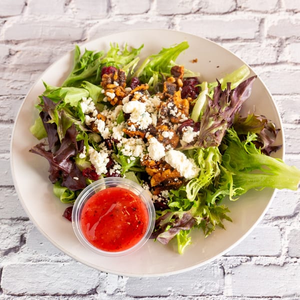 Angel Fired Pizza's mixed green salad with feta, candied nuts, dried cranberries, and a side of dressing.