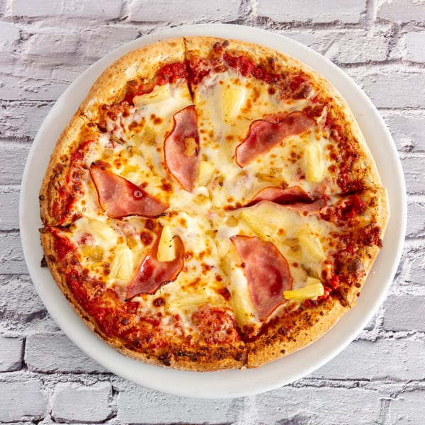 Angel Fired Pizza's Hawaiian pizza, topped with ham, pineapple, and melted cheese on a white plate.