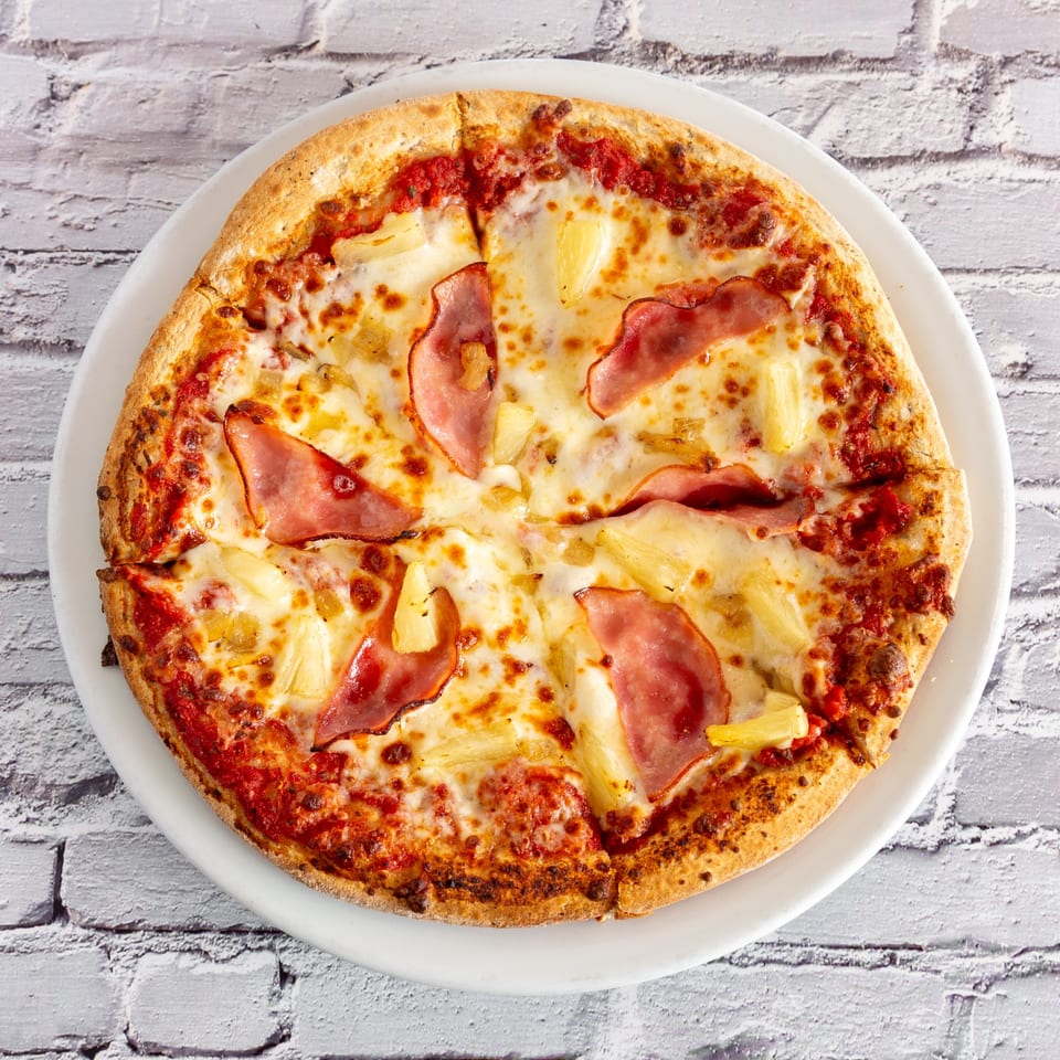 Angel Fired Pizza's Hawaiian pizza, topped with ham, pineapple, and melted cheese on a white plate.